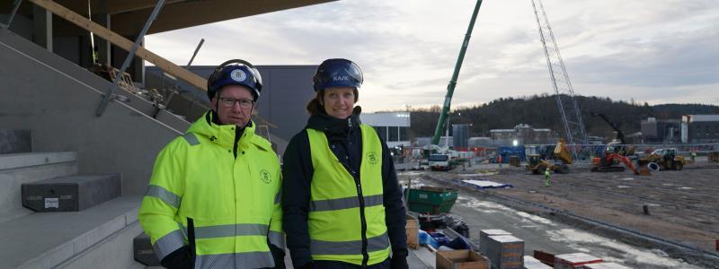 Projektledarna Anders Emilsson och Cecilia Wahlskog på den Östra läktaren av Rimnersvallen, i bakgrunden syns det första belysningstornet komma på plats. Foto: Uddevalla kommun