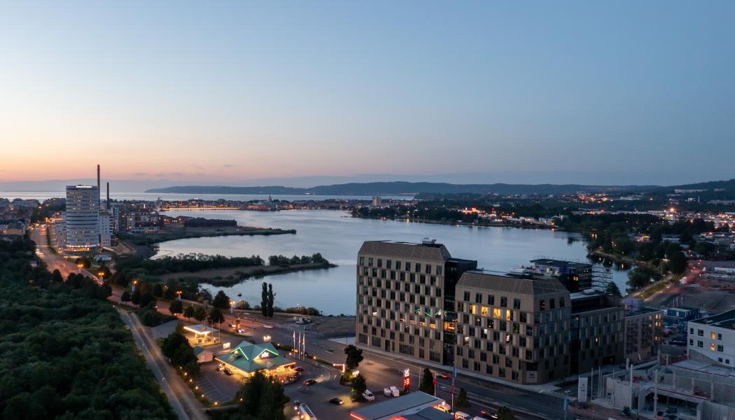 Kvällsvy över det nio våningar höga kontorshuset med Munksjön och Vättern i bakgrunden. Bild: Skanska