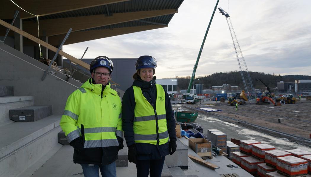 Projektledarna Anders Emilsson och Cecilia Wahlskog på den Östra läktaren av Rimnersvallen, i bakgrunden syns det första belysningstornet komma på plats. Foto: Uddevalla kommun
